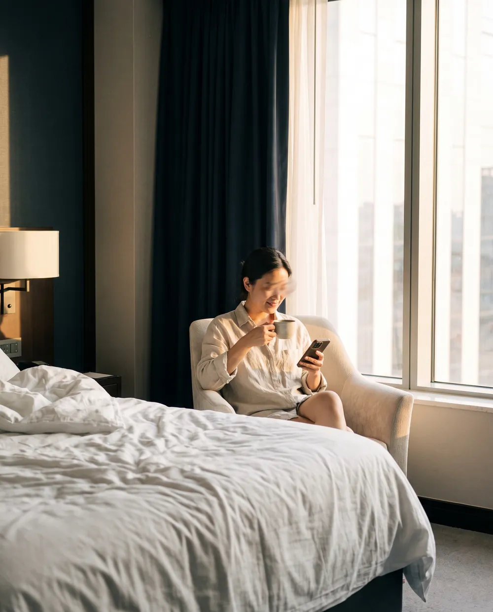 A guest with a coffee reading on a phone by a hotel window